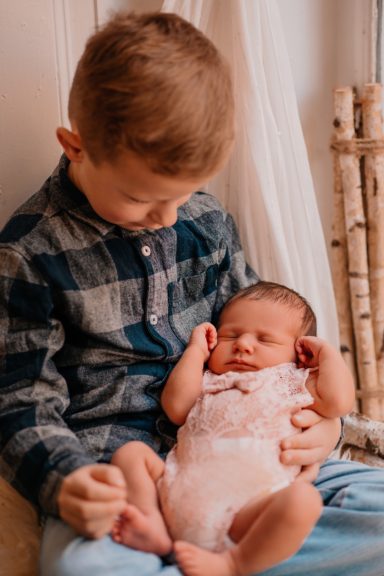 Ein Junge sitzt und hält ein neugeborenes Baby in seinen Armen.