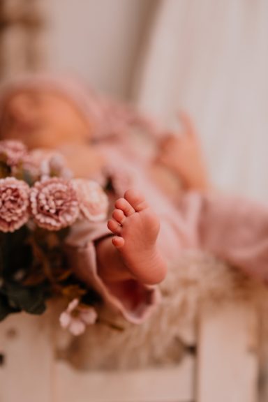 Füße eines schlafenden Babys, umgeben von rosa Blumen.