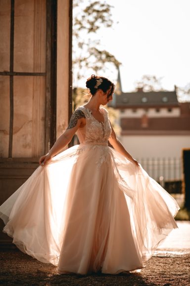 Frau in einem eleganten, fließenden Hochzeitskleid vor einem sonnendurchfluteten Hintergrund.