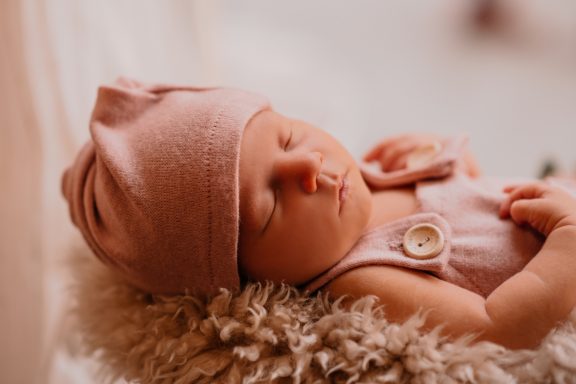 Neugeborenes Baby schläft friedlich in einem rosa Hut und Anzug.
