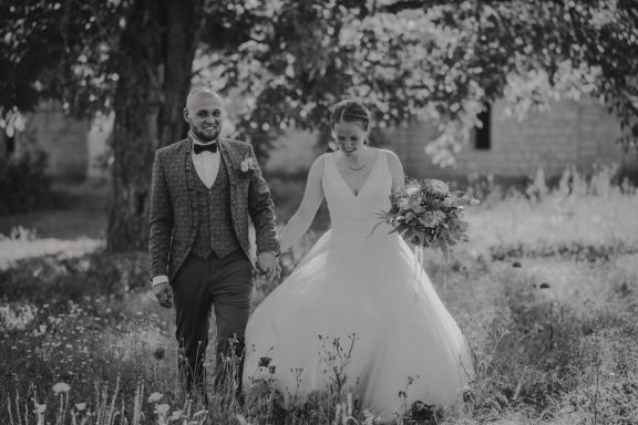 Braut und Bräutigam in Hochzeitskleidung, Hand in Hand in einer blühenden Wiese.