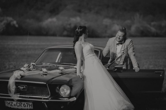 Braut und Bräutigam posieren vor einem klassischen Auto in einer romantischen Szene.