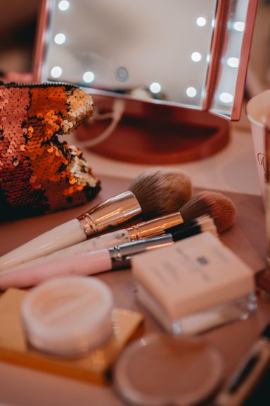 Make-up Pinsel und Kosmetikprodukte auf einem Tisch vor einem beleuchteten Spiegel.