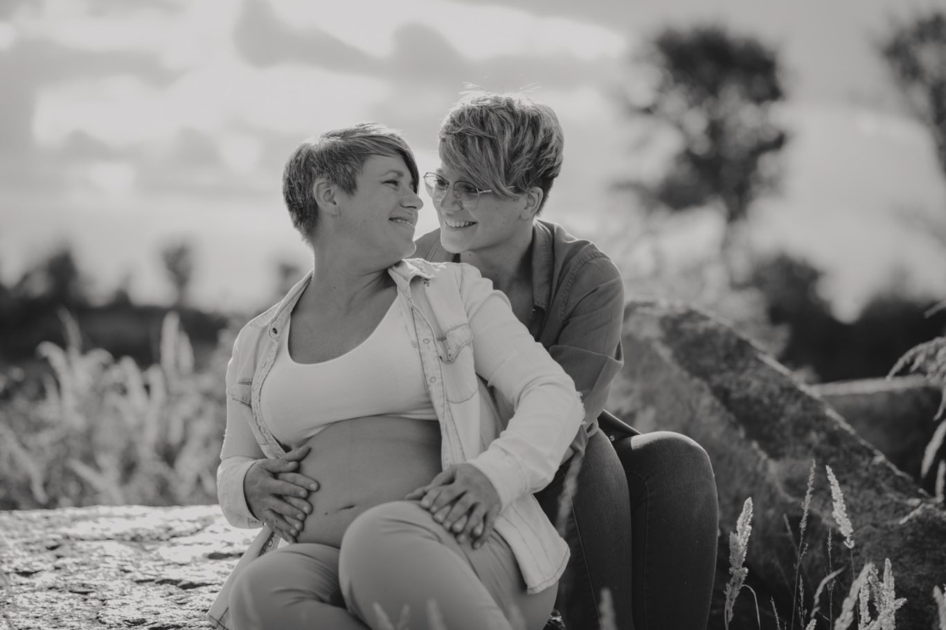 Zwei Frauen sitzen eng beieinander in einer natürlichen Umgebung.