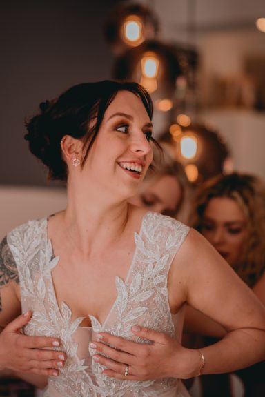 Eine Braut in einem weißen Kleid mit strahlendem Lächeln, begleitet von Freunden.