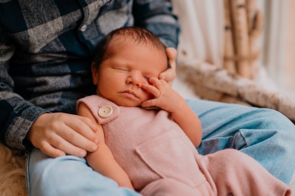 Neugeborenes Baby in rosa Overall schläft auf dem Schoß einer Person.