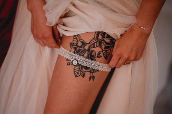 Tattoo aus schwarzen Blumen und Linien auf dem Oberschenkel, mit einem weißen Strumpfhalter.