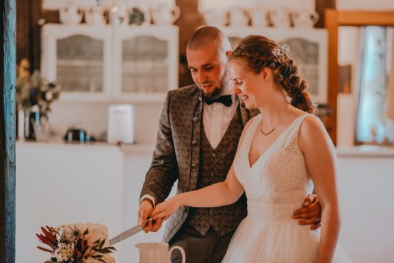 Ein Brautpaar schneidet gemeinsam eine Hochzeitstorte in einem festlichen Raum.