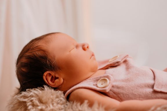 Schlafendes Baby in rosa Kleidung mit zartem Gesichtsausdruck auf einem weichen Untergrund.