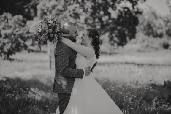 Hochzeitspaar umarmt sich liebevoll vor einer blühenden Kulisse.