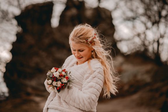Junge Frau mit langen blonden Haaren hält einen Blumenstrauß vor einer natürlichen Kulisse.