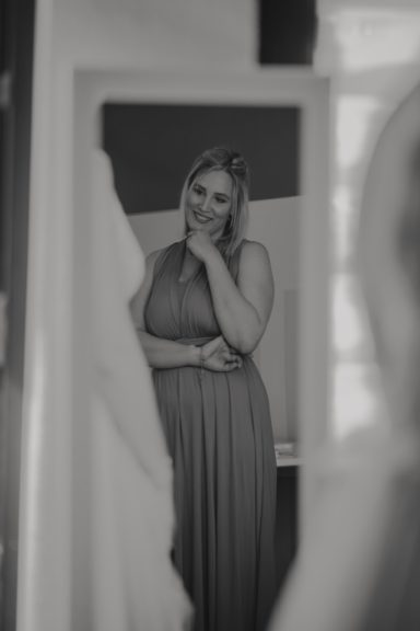 Frau in einem langen Kleid, die nachdenklich in einen Spiegel schaut.