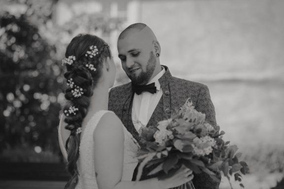 Brautpaar in eleganter Kleidung, lächelnd und umgeben von Blumen.