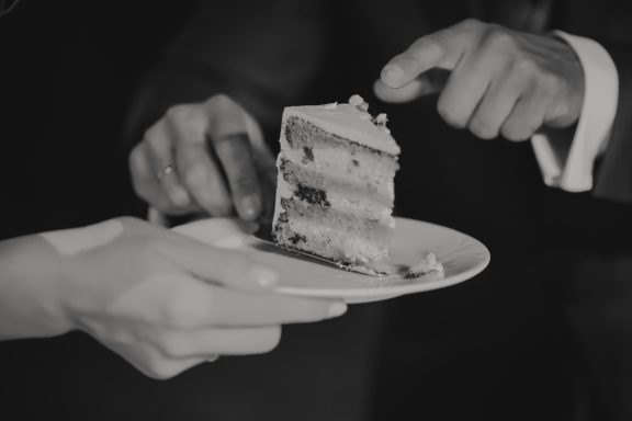Zwei Hände reichen ein Stück Torte auf einem weißen Teller.