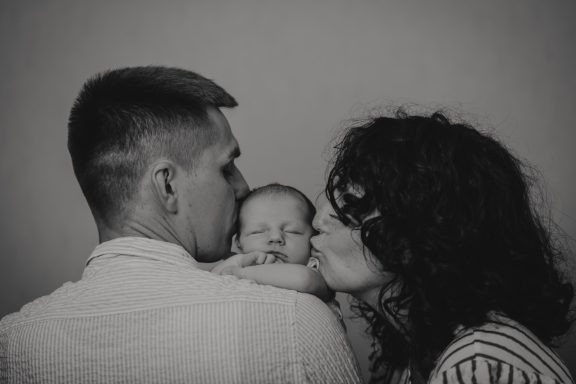 Familie mit einem Baby, Eltern küssen sich, das Baby in der Mitte.