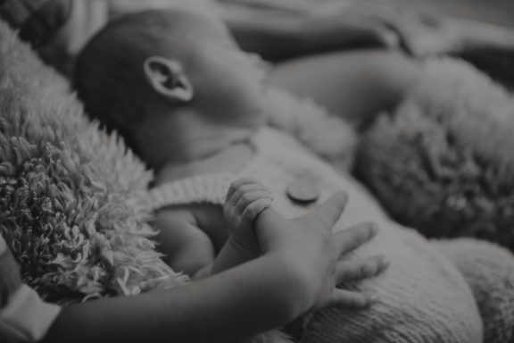 Schlafendes Baby, sanft gehalten von einer Person, umgeben von Kuscheltieren.