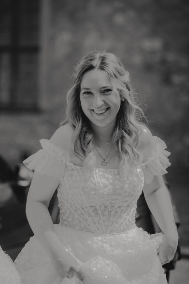Lächelnde Frau in einem Brautkleid mit Rüschenärmel und lockigem Haar.
