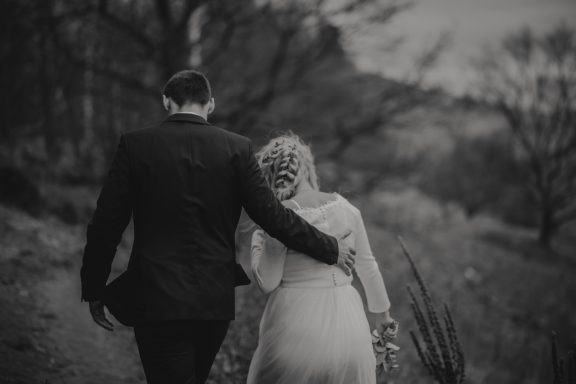 Brautpaar, Hand in Hand, spaziert in einer landschaftlichen Umgebung.