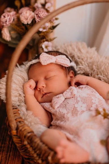 Schlafendes Baby in einem Körbchen mit Blumen und einer Schleife im Haar.